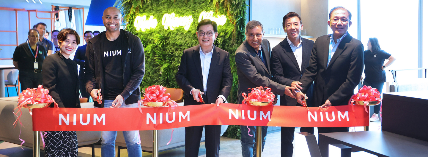People cutting a NIUM-branded red ribbon at an office opening.